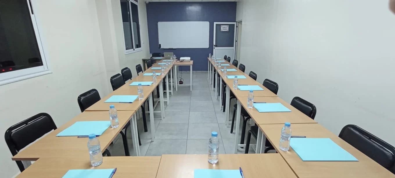 طاولات مرتبة على شكل حرف U وسبورة وجهاز عرض داخل قاعة المركز